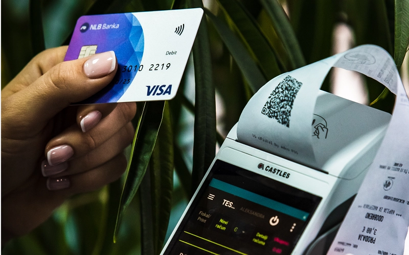 enupay2 Ruka osobe koja drzi platnu karticu pored ENU uredjaja iz kog je izasao racun